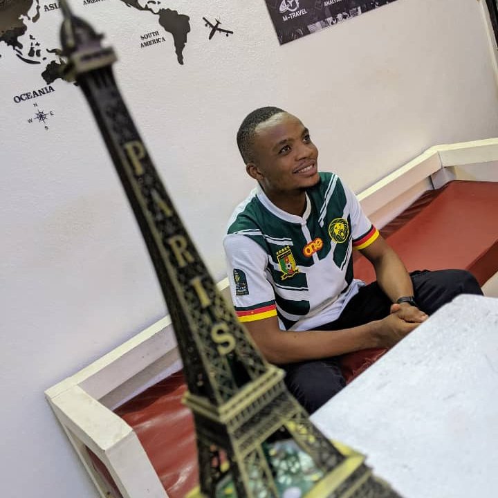 Client de Merlo Skills Group dans notre agence de billetterie aérienne au Cameroun, entouré d'une carte du monde et d'une maquette de la Tour Eiffel, symbole des voyages internationaux vers la France et l'Europe.
