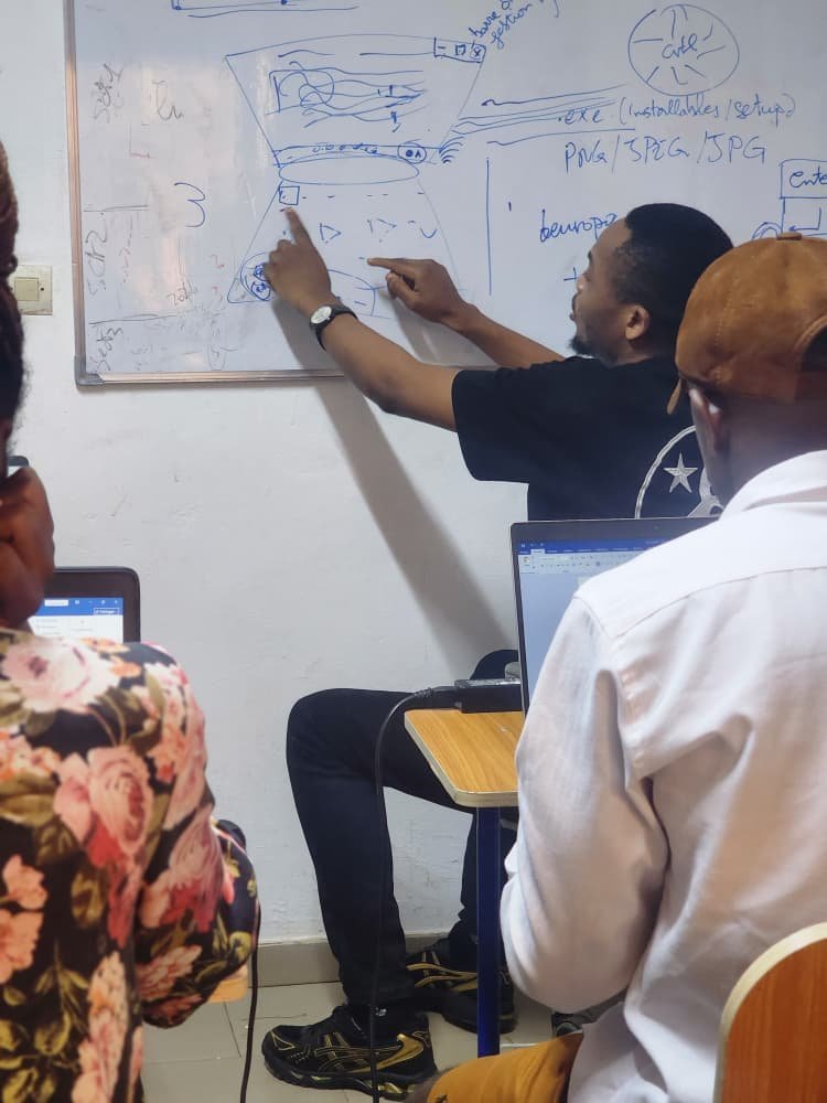 Formateur détaillant un schéma de gestion de base de données au tableau pour des apprenants en formation informatique.